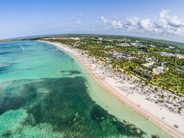 Un resort costero con una playa de arena, palmeras y aguas turquesas cristalinas.