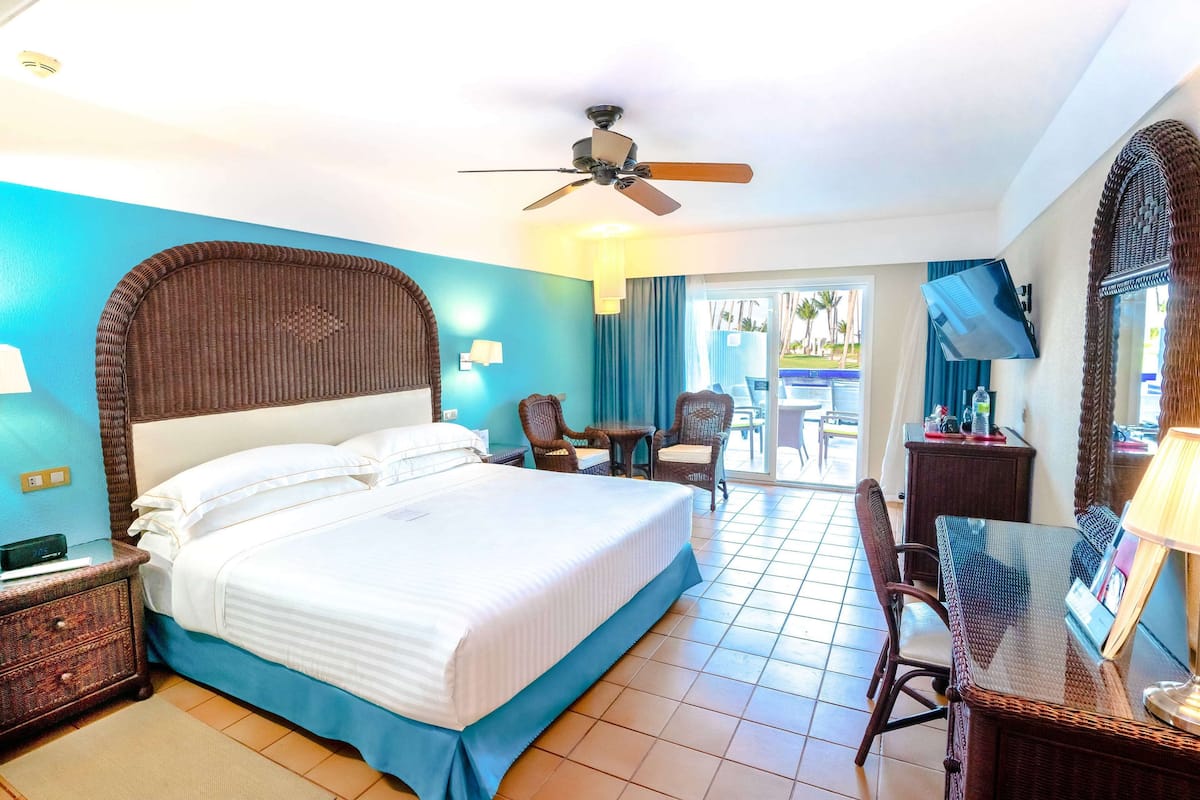A hotel room with a large bed, a desk with a chair, a TV, and a balcony with a view.