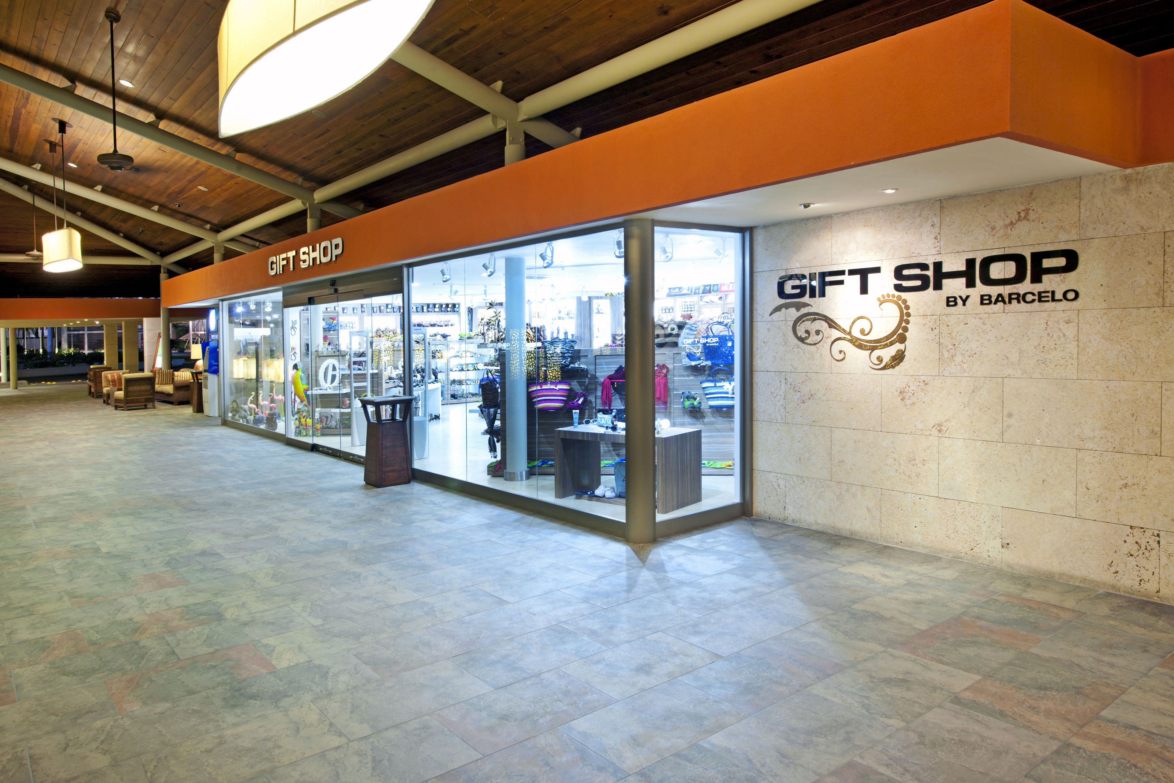 A gift shop with a clear glass front, located in a spacious indoor area with tiled flooring and wooden ceiling beams.