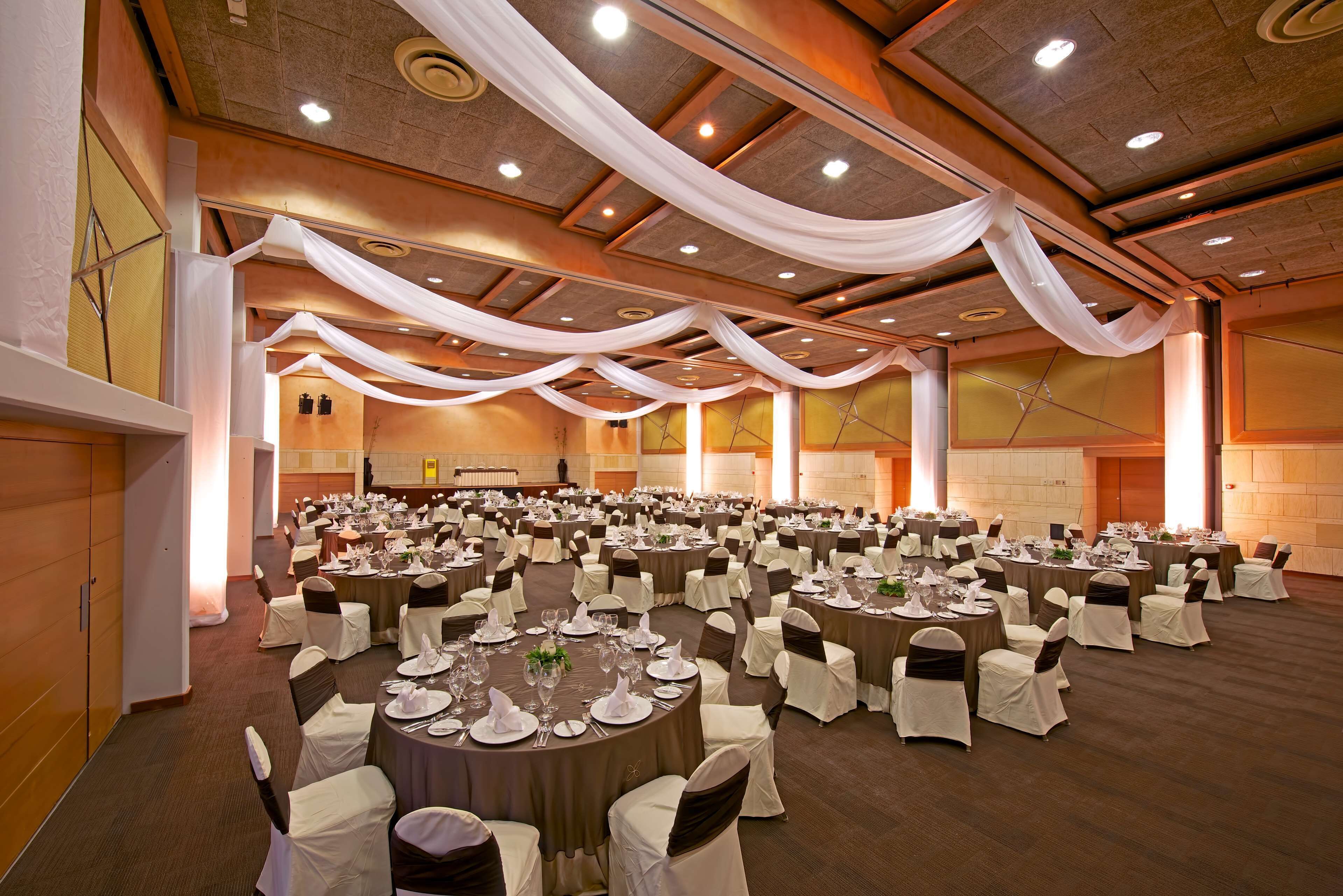 Une grande salle de banquet avec des tables rondes, des nappes blanches et des rubans noirs décorant les chaises.