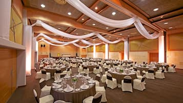 Une grande salle de banquet avec des tables rondes, des nappes blanches et des rubans noirs décorant les chaises.