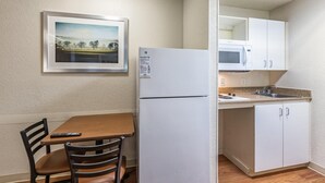 Eine kleine Küchenzeile mit Kühlschrank, Mikrowelle und Spüle. An der Wand hängt ein gerahmtes Bild und es gibt einen Tisch mit Stühlen.