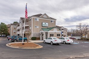 Een meerhoog hotel met een bord waarop 'Home Towne Studios Red Roof' staat. Er staan auto's op de oprit en een vlaggenmast met de Amerikaanse vlag.