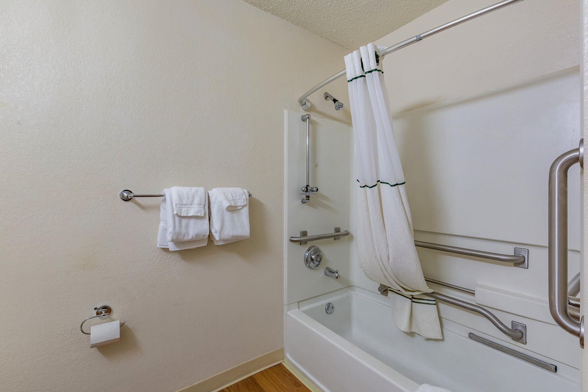 A bathroom with a shower, grab bars, and a towel rack.