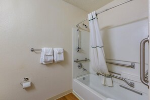 A bathroom with a shower, grab bars, and a towel rack.
