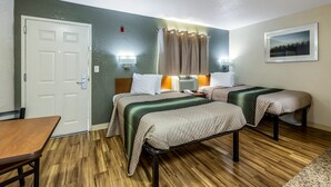 Ein Hotelzimmer mit zwei Betten, einem Holztisch, einer Tür und einem an der Wand hängenden Bild.