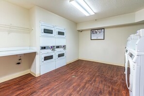 A laundry room with stacked washers and dryers, a white wall-mounted oven, and a framed informational poster. - HomeTowne Studios By Red Roof Gainesville, GA (Gainesville)