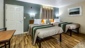 Ein Hotelzimmer mit zwei Betten, Holzboden, einer weißen Tür, einem Tisch und einem Wandbild.