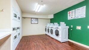 Une buanderie équipée de plusieurs machines à laver, d’une caméra de surveillance et d’une affiche encadrée accrochée au mur.