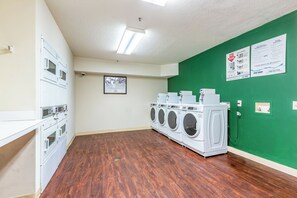 A laundry room with multiple washing machines, a security camera, and a framed poster on the wall.