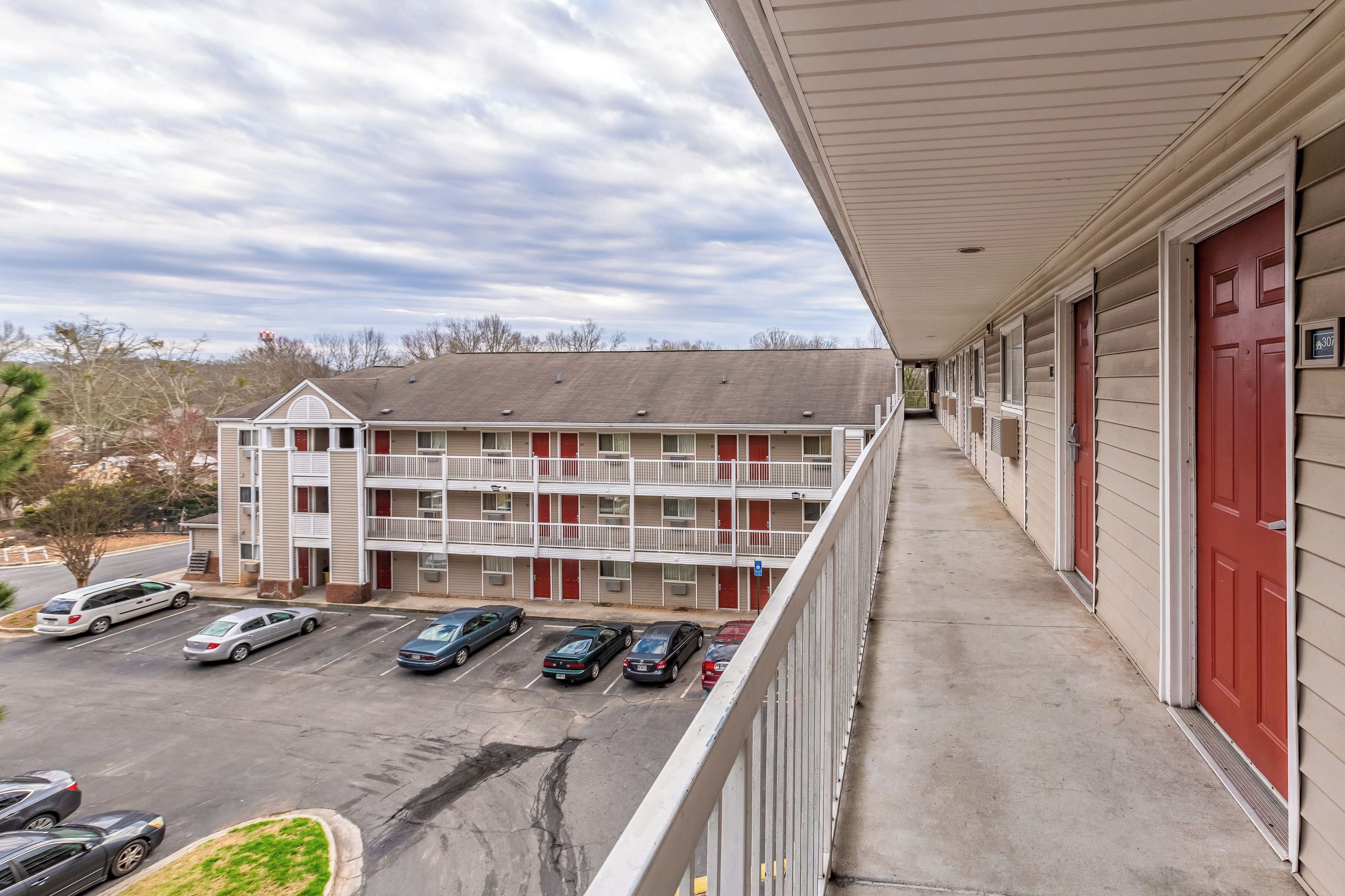 A multi-story motel with a parking lot, a covered walkway, and a view of the surrounding area.