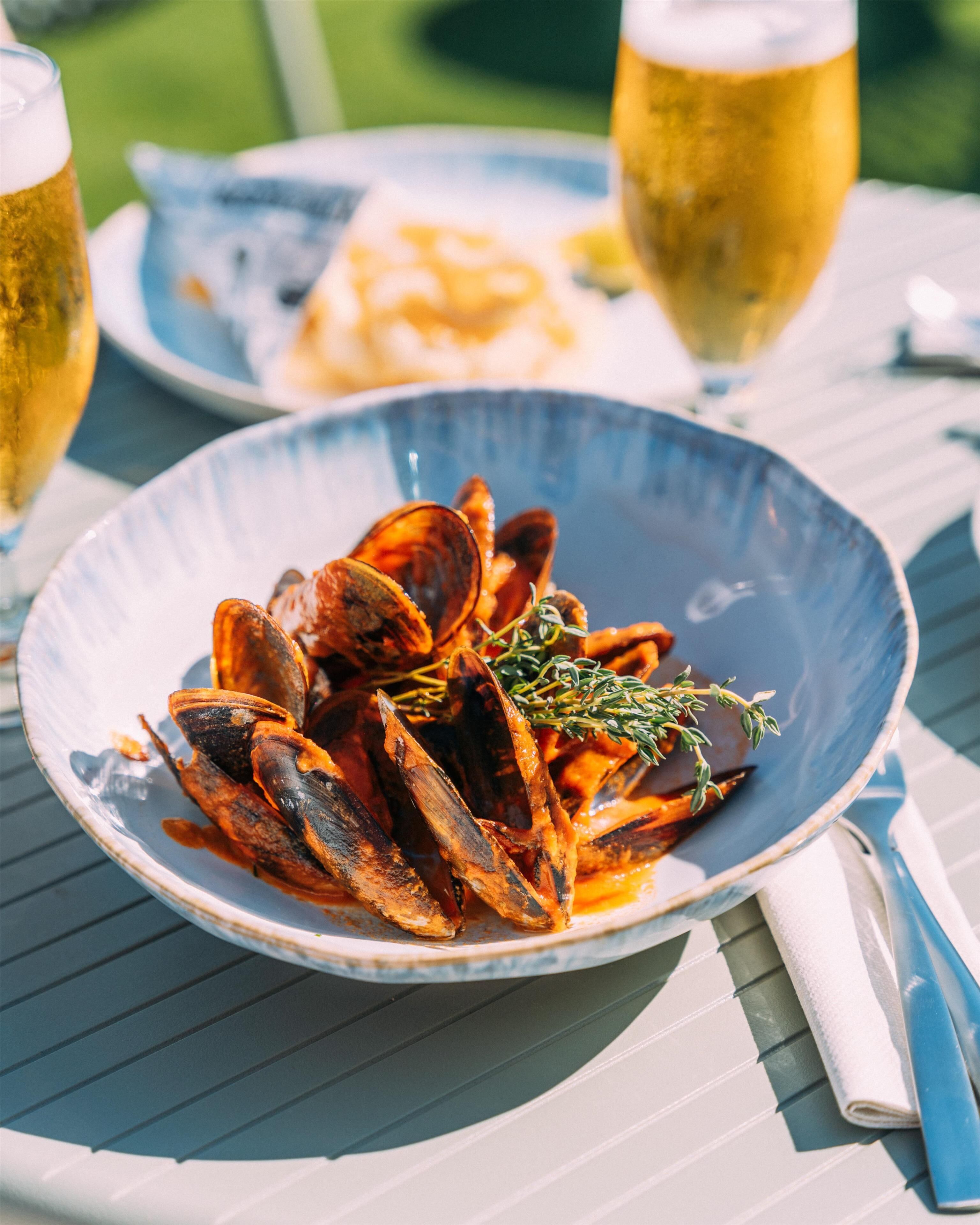 A table with a plate of mussels and a glass of beer.
