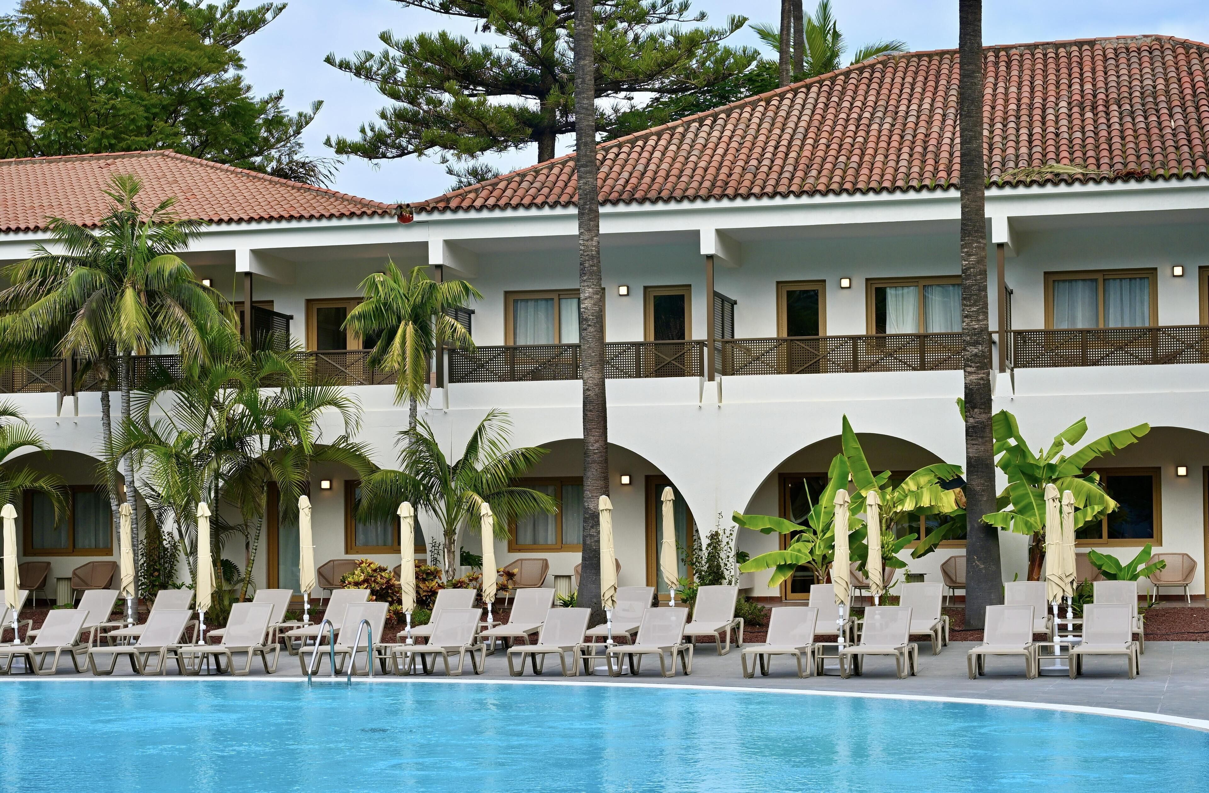 A hotel with a swimming pool, lounge chairs, and palm trees.