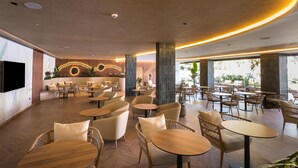 A spacious indoor area with multiple seating arrangements, including round tables and wicker chairs, and a large flat-screen TV mounted on the wall. - Radisson Resort & Residences Tenerife - Adults Only (Puerto de la Cruz)