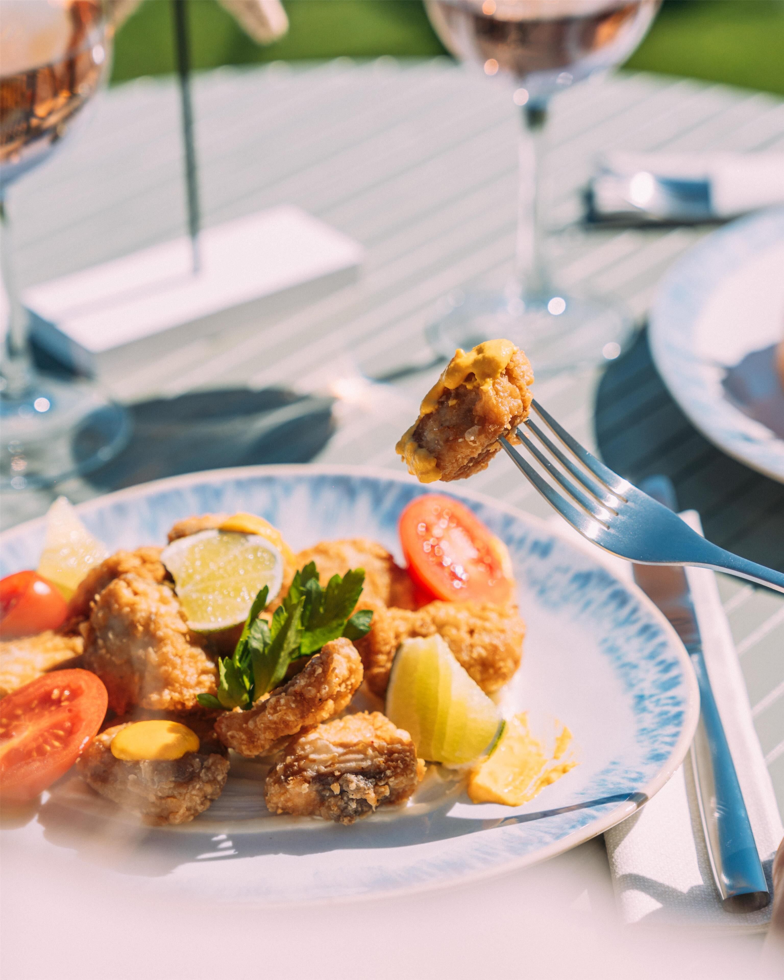 Een bord met gefrituurd eten, citroenpartjes en peterselie, geserveerd op een witte tafel met een blauw patroon.