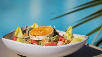 Un bol de salade surmonté d’une tranche de fromage, posé sur une table devant un fond bleu.