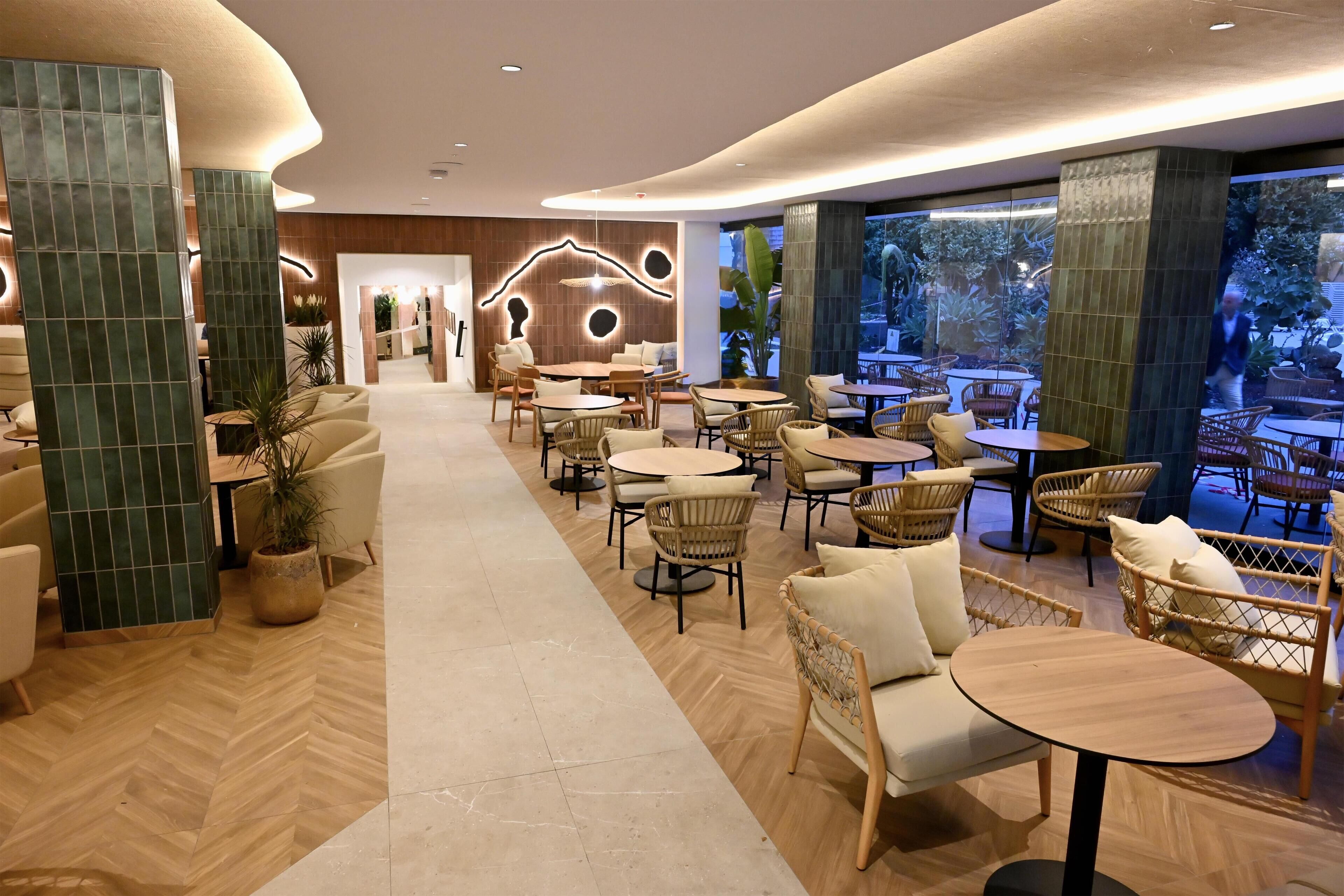 A modern interior with a central walkway, round tables, wicker chairs, and a view of the outdoors.