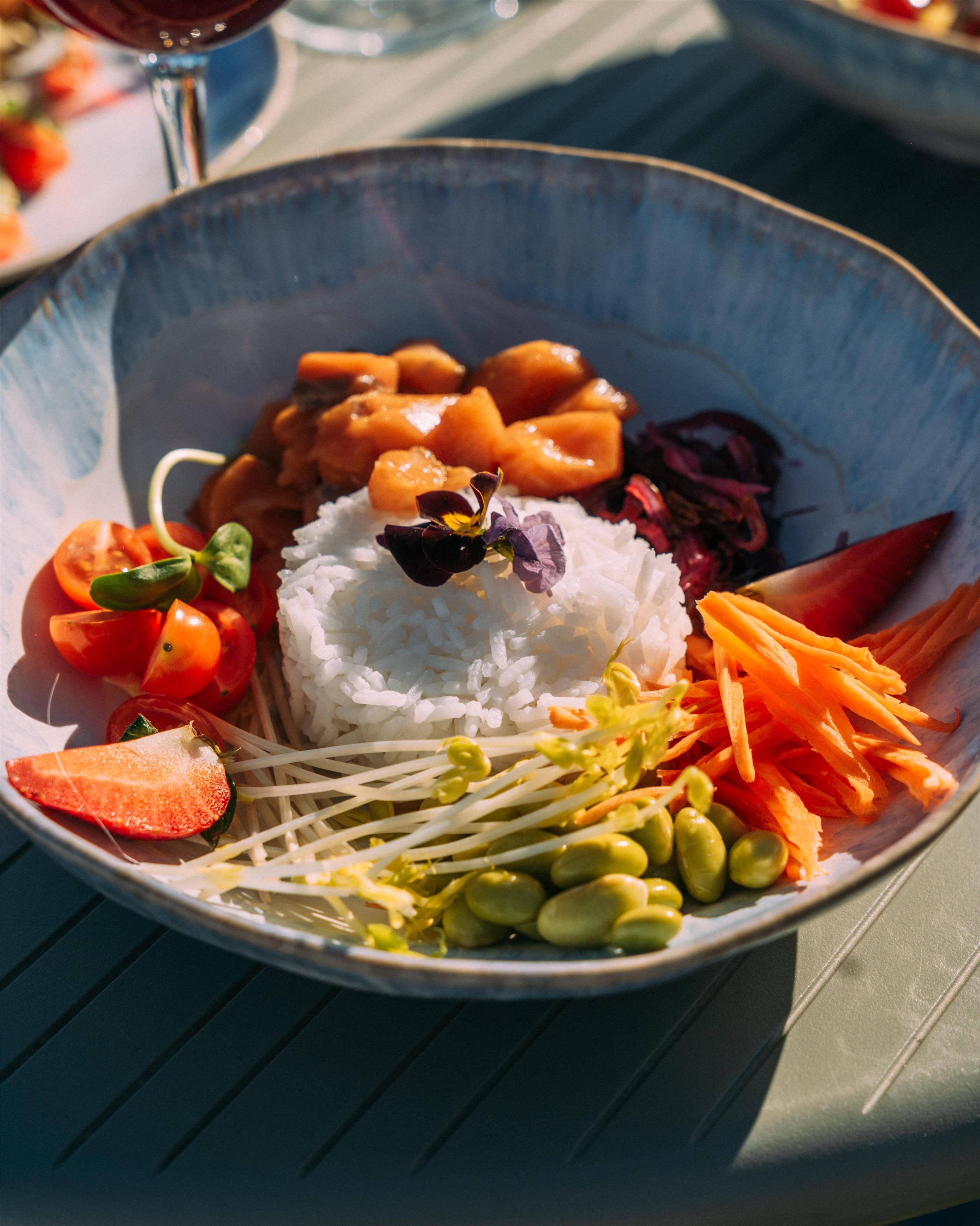 A bowl of rice with vegetables and a flower on top.
