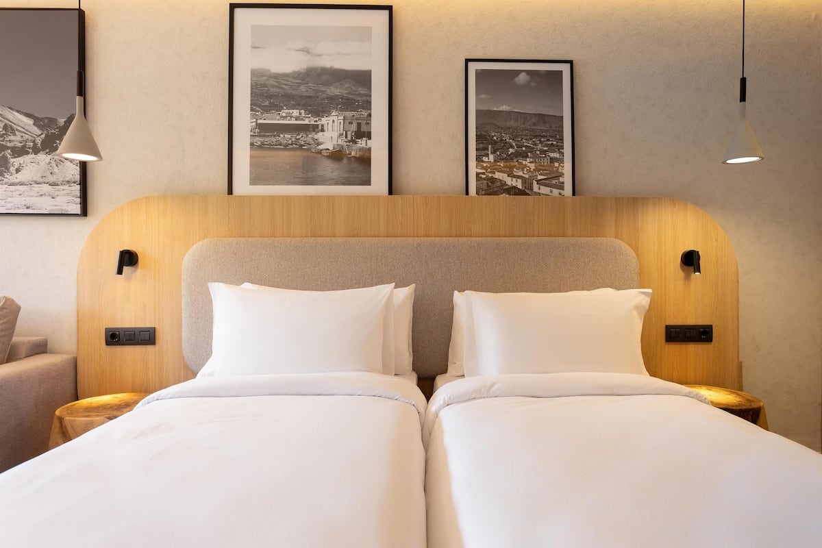 Una cama doble con ropa de cama blanca, un cabecero de madera y dos mesitas de noche con lámparas.