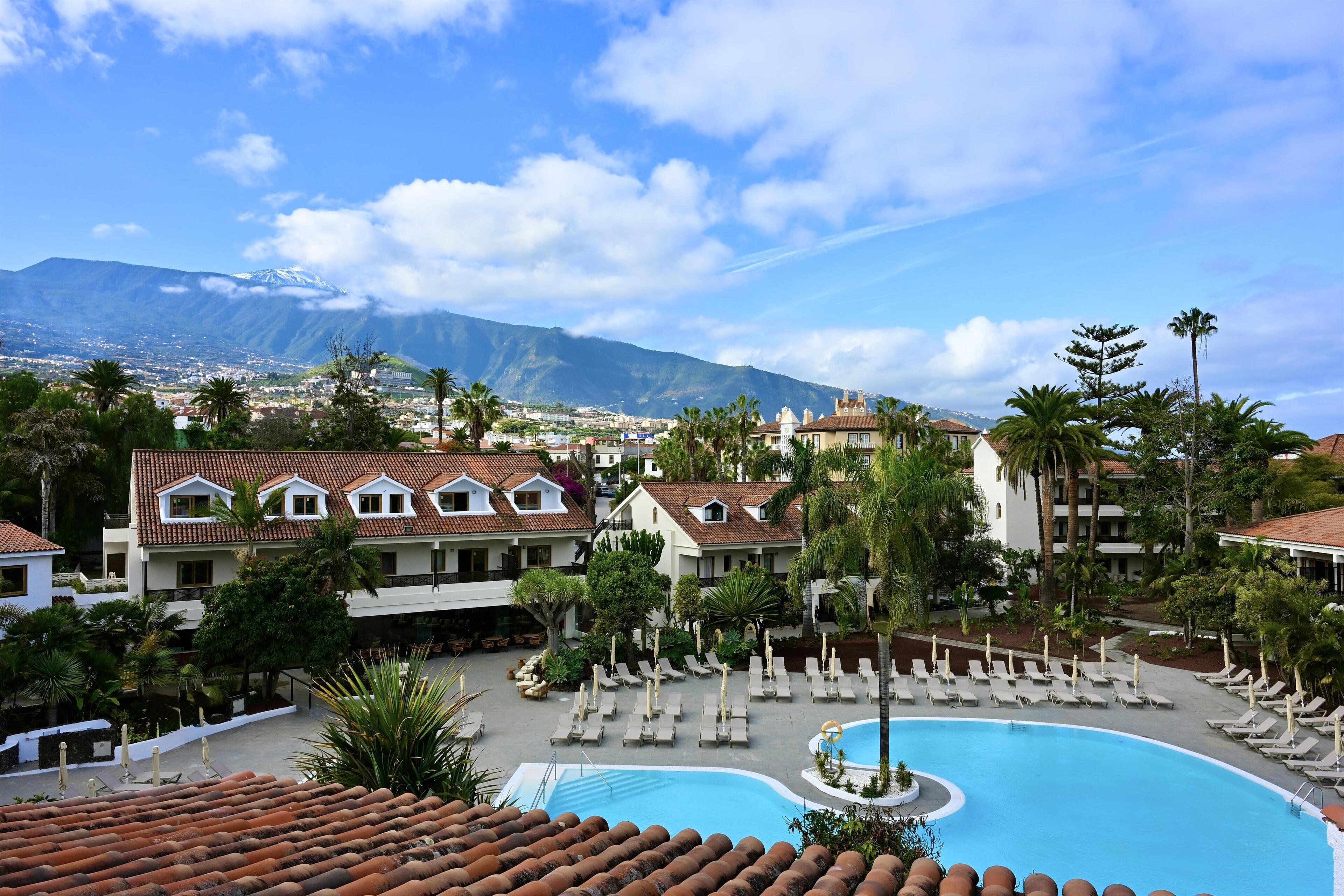 Un resort con piscina, palmeras y una montaña al fondo.