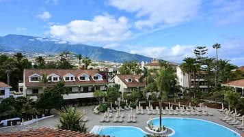 Un resort con piscina, palmeras y una montaña al fondo.