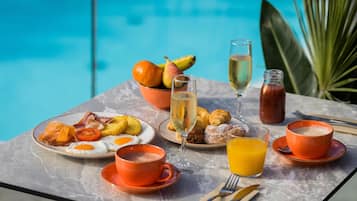 Una mesa de desayuno con platos de comida, bebidas y vista a una piscina.