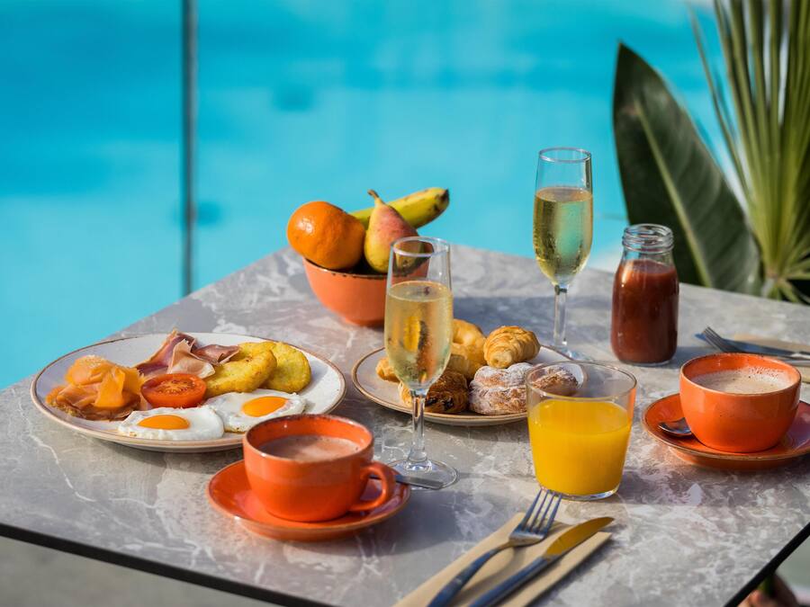 Una mesa de desayuno con platos de comida, bebidas y vista a una piscina.