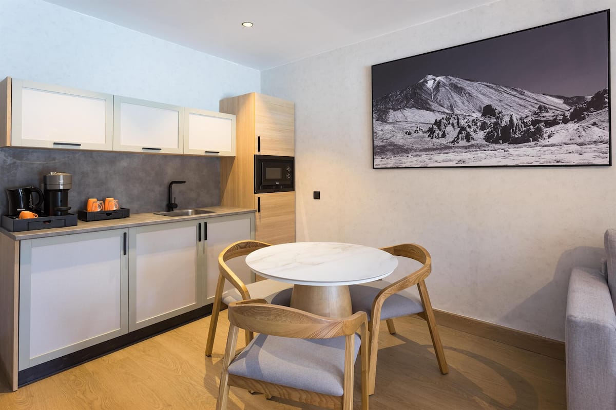Una cocina moderna con armarios de madera, una mesa redonda con sillas y un cuadro en la pared.