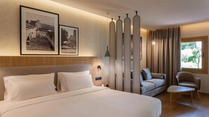 A hotel room with a large bed, a sofa, a chair, and a window with curtains. - Radisson Resort & Residences Tenerife - Adults Only (Puerto de la Cruz)
