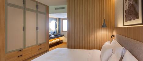 A hotel room with a large bed, wooden wardrobe, a vanity with a mirror, and a framed picture on the wall.