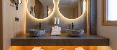 A modern bathroom with two round mirrors, a wooden vanity, and a shelf with towels.