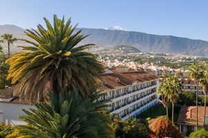 Un hotel de estilo arquitectónico tradicional, con un patio con palmeras y vistas a una montaña.