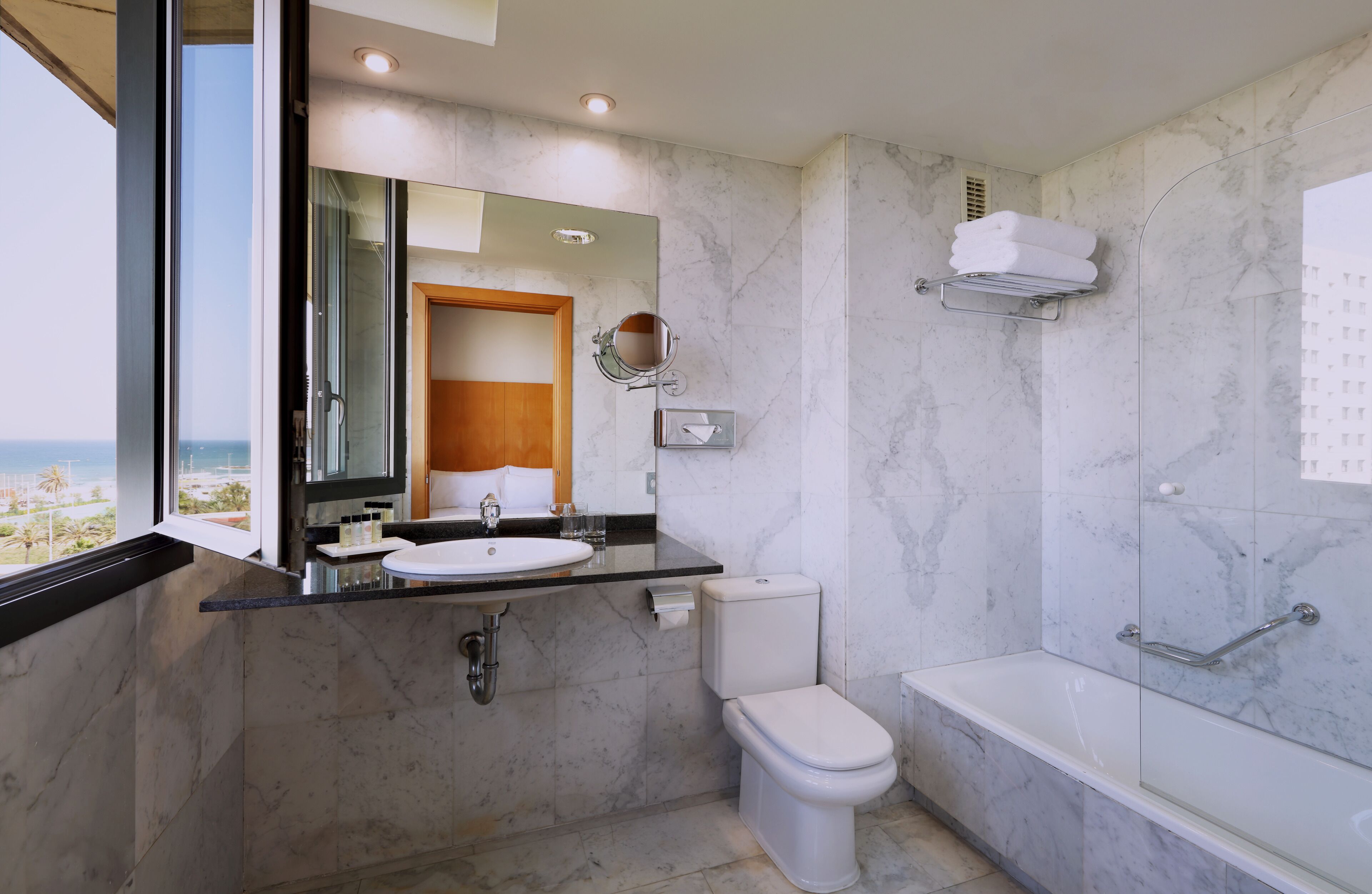 A modern bathroom with a large mirror, a toilet, a sink, and a bathtub.