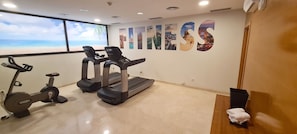 A fitness room with treadmills, an elliptical, and a large window with a beach view. - Catalonia Barcelona Beach (Barcelona)
