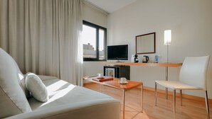 A modern hotel room with a sofa, a small table, a TV, a coffee machine, and a chair. - Catalonia Barcelona Beach (Barcelona)