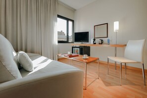 A modern hotel room with a sofa, a small table, a TV, a coffee machine, and a chair. - Catalonia Barcelona Beach (Barcelona)
