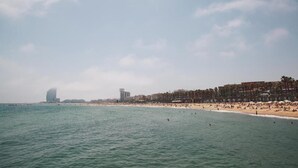 A beach with a clear view of the ocean and a row of buildings in the background. - Catalonia Barcelona Beach (Barcelona)