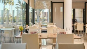 A modern dining area with glass partitions, white chairs, and tables set for dining. - Catalonia Barcelona Beach (Barcelona)