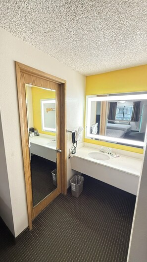 A bathroom with a wooden door, a sink, a mirror, and a trash bin.