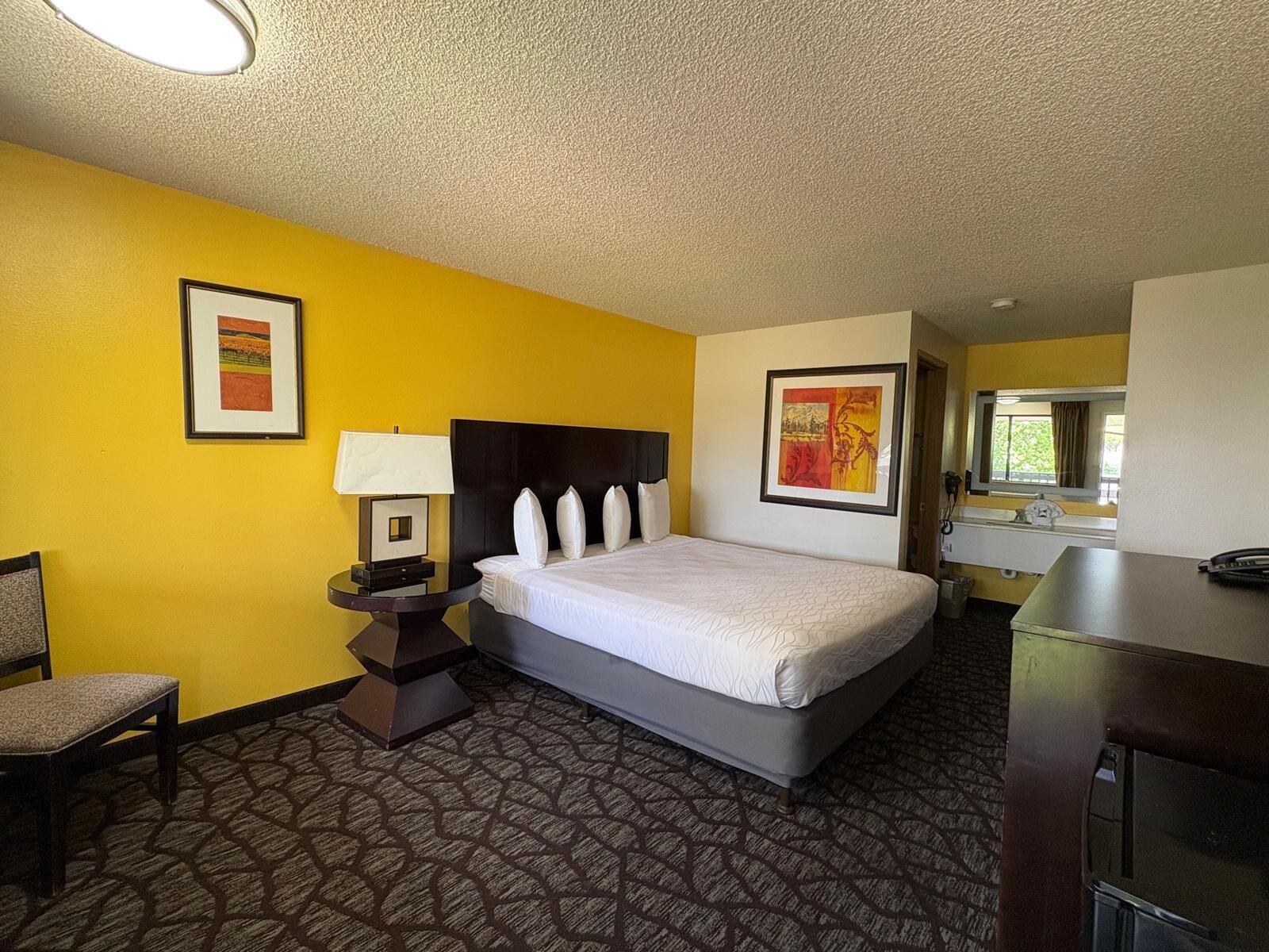 A hotel room with a bed, a chair, a desk, and a bathroom visible through an open door.