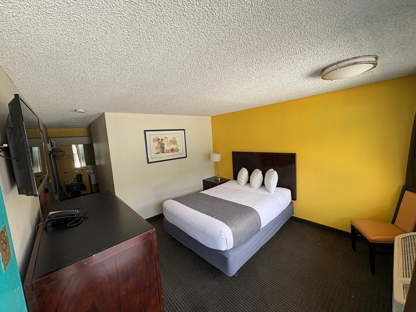 A hotel room with a bed, a desk, a chair, a picture on the wall, and a ceiling light.