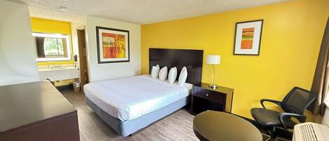 A hotel room with a bed, bedside table, chair, desk, and a window.