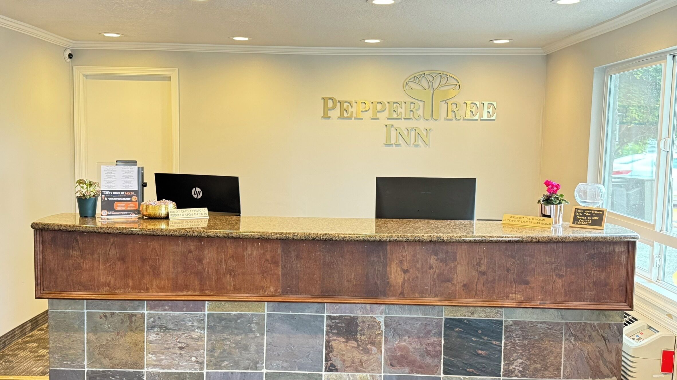 A hotel reception desk with a stone tile base, a computer, a plant, and a sign reading "PepperTree Inn".