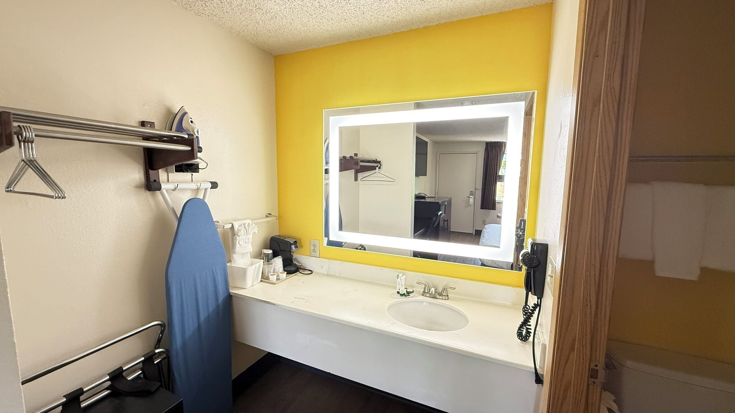 A bathroom with a yellow accent wall, a large mirror, a sink, and a hanging towel rack.
