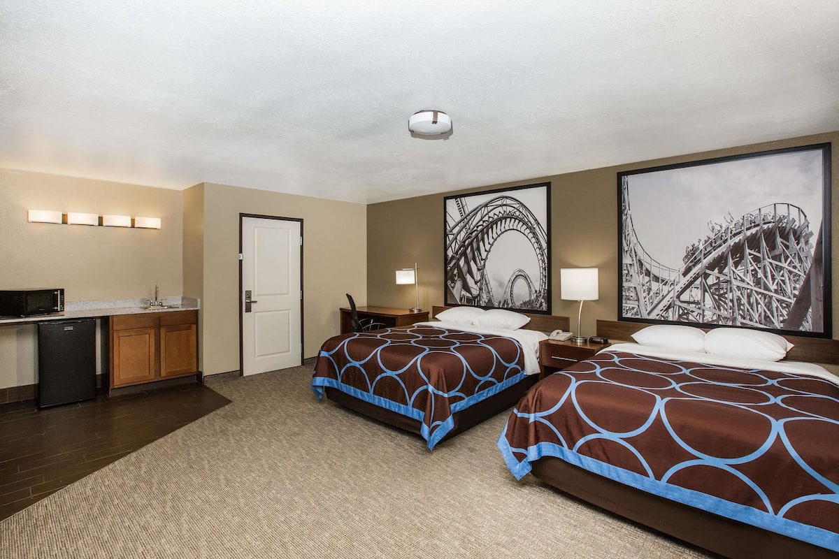 Habitación de hotel con dos camas, un escritorio con microondas, una puerta y dos luces fijadas a la pared.