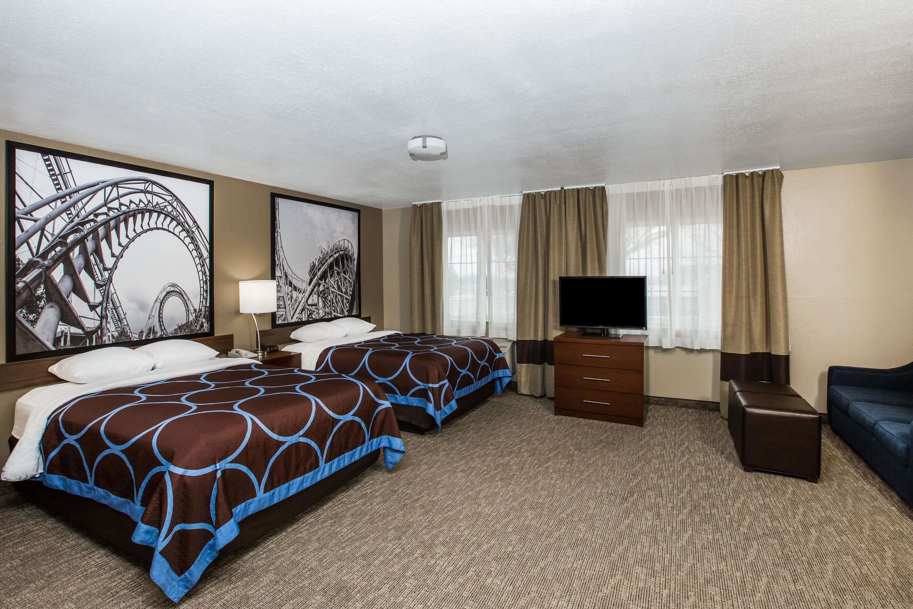 Une chambre d’hôtel avec deux lits, une télévision, une commode et une grande fenêtre avec des rideaux.