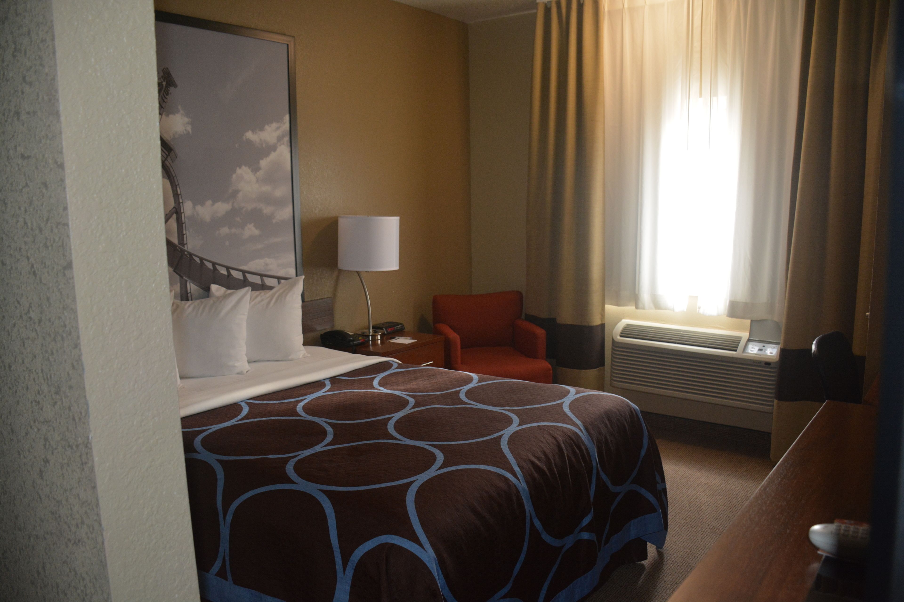 Une chambre d’hôtel avec un grand lit, un bureau, une chaise, une lampe et une fenêtre avec des rideaux.