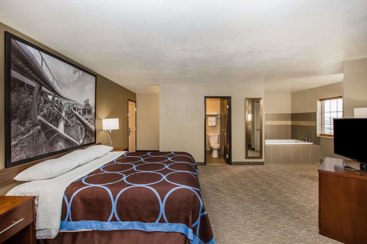 Habitación de hotel con una cama grande, televisión, baño con bañera y un pasillo que conduce a otra habitación.