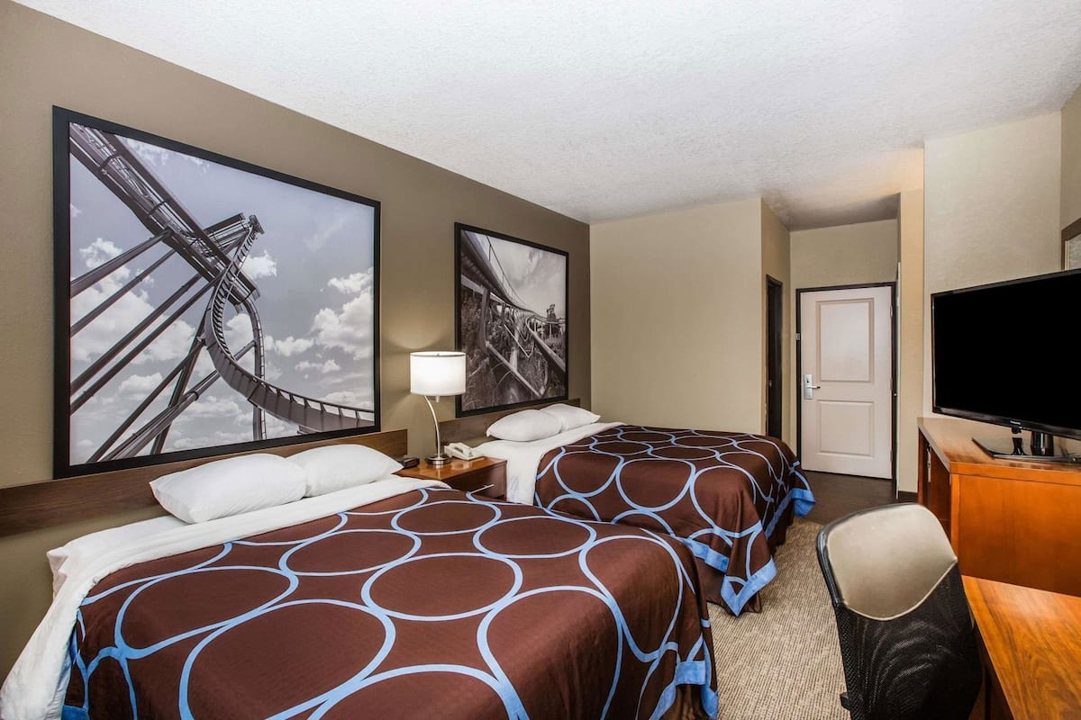 Habitación de hotel con dos camas, televisión, escritorio y ventanas amplias con vista a un puente.