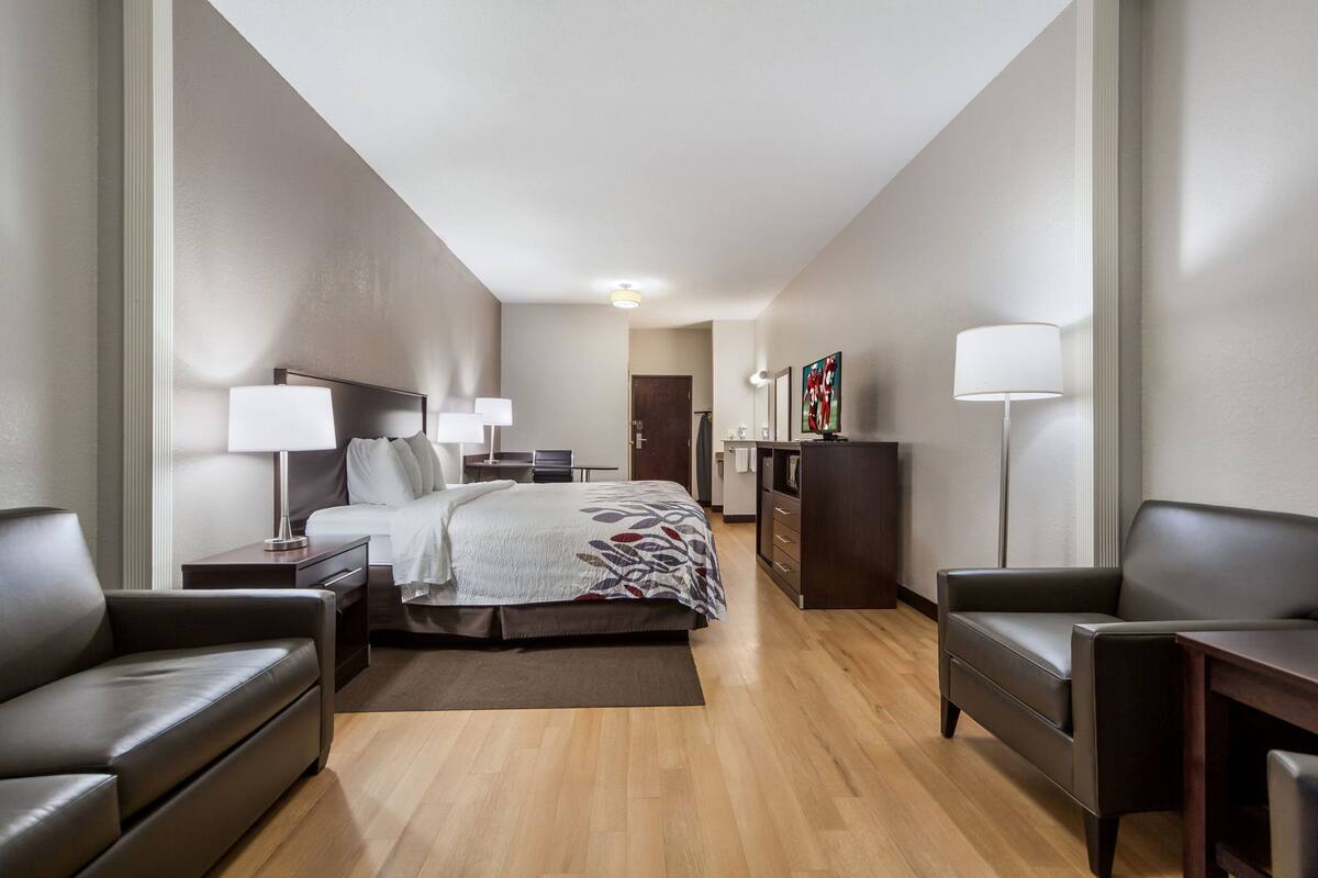 Une chambre d’hôtel comprenant un lit, deux chaises, un bureau, une commode et un téléviseur à écran plat.